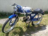 une moto bleue garée sur l'herbe près d'un mur