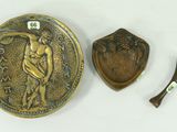 une plaque en bronze et une cuillère en bois posées sur une surface blanche