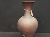 un vase marron posé sur une surface noire, près d'un mur noir