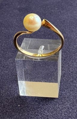 bague plaquée or ornée d'une perle blanche sur un socle en acrylique transparent