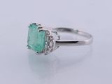 an emerald and diamond ring on a white surface