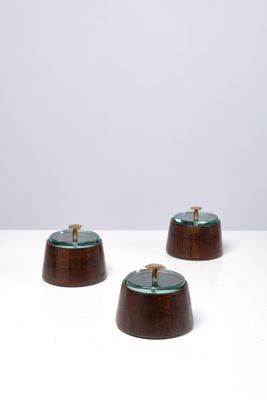 trois petits bols en bois avec des couvercles en verre, posés sur une surface blanche