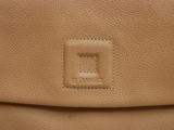 the back view of a tan leather purse with a small square logo on it