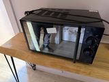a microwave sitting on a table with a person standing in the reflection of it