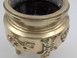 a small brass pot on a stand on a white surface
