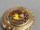 a close up of a gold broochle with a yellow stone in the center
