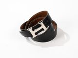 une ceinture en cuir noir avec une boucle argentée sur fond blanc