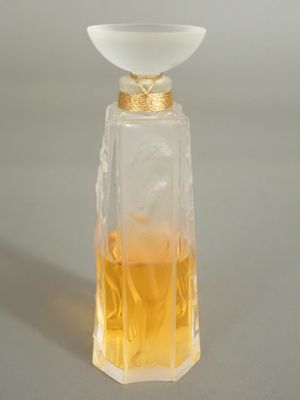 flacon de parfum avec un bouchon en verre et un bord doré sur un fond gris