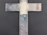 a metal cross hanging from a chain on a black surface