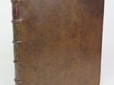 an old brown book sitting on top of a table next to a white wall