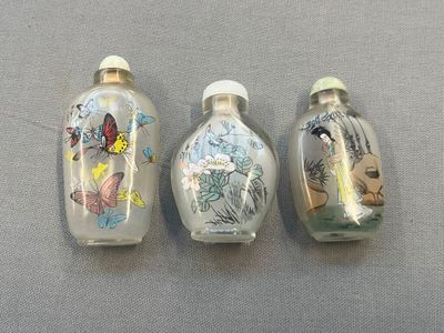 trois flacons à tabac en verre posés sur une table, ornés de papillons