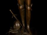 bronze statue of a man in armor holding a sword and a book