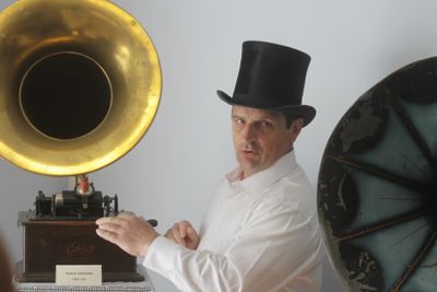 un homme coiffé d'un haut-de-forme, debout devant un gramophone