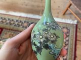 a person holding a green vase with flowers on it