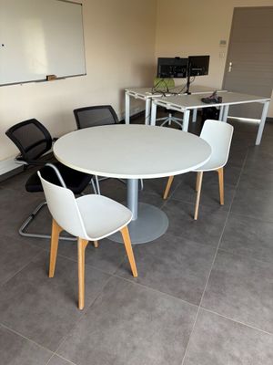 une table et des chaises blanches dans une salle équipée d'un tableau blanc