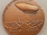 une image représentant une médaille de bronze sur laquelle figure un dirigeable survolant un navire