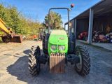 un tracteur vert garé devant un bâtiment, à côté d'un tas de terre