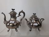 two silver teapots on display on a glass shelf