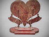 sculpture of a red heart on a wooden base with two crossed arrows