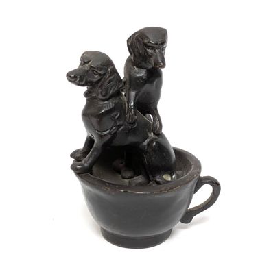 statue of two dogs sitting in a cup on a white surface