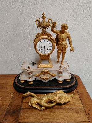 une horloge posée sur une table, surmontée d'une statue