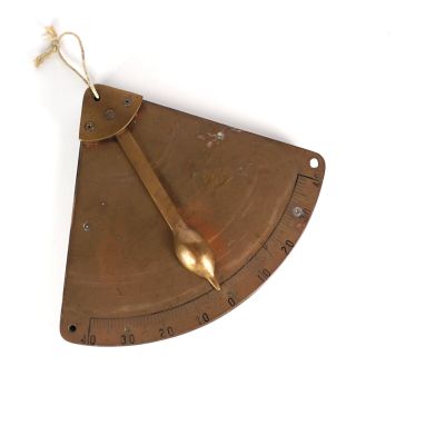 un cadran solaire en laiton posé sur une surface blanche, avec une cuillère en or