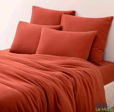 une photo d'un lit avec des draps et des oreillers orange
