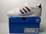 une paire de baskets Adidas blanches et bordeaux posée sur une boîte bleue