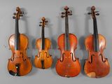 four old violins are lined up against a gray wall