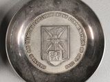 two silver plates with a medal on top of them on a white surface