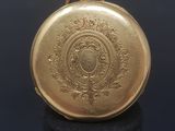 an antique gold pocket watch on a black stand against a dark background