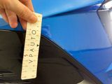 a hand that is holding a ruler in front of a blue car