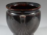 a black vase with a brown rim sitting on a white surface