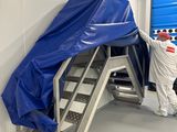 des ouvriers en tenue de protection descendent un grand panneau par un escalier