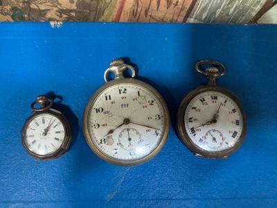 three antique pocket watches are sitting on a blue surface
