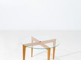 une table avec un plateau en verre et des pieds en bois dans une pièce blanche