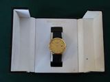a gold watch in a black box on a green surface