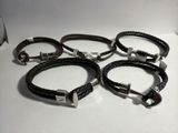 six bracelets en cuir noir avec des fermoirs en argent, posés sur un fond blanc