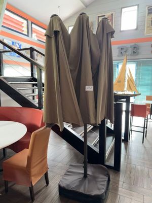 tables and chairs with umbrellas on them in a room with a staircase
