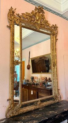 a mirror on a mantle in a room with a chandelier in the background
