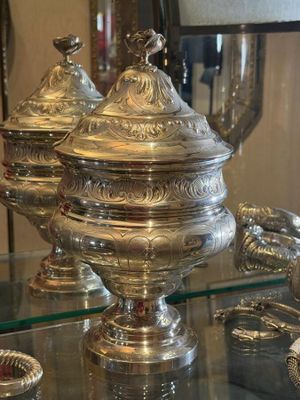 a glass table with silver dishes on it and a lamp in the background
