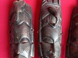 three wooden masks are sitting on a pink cloth on a table