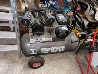 un petit compresseur d'air posé dans un garage à côté d'un tas de vieilleries
