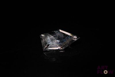 un gros plan d'un diamant posé sur une surface noire, avec un fond noir
