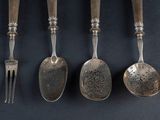 four spoons and a fork are lined up on a black surface