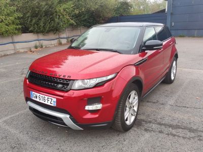Le Range Rover rouge est garé sur un parking devant un immeuble.
