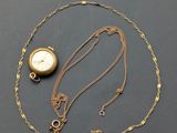 a close up of a gold necklace with a clock on it