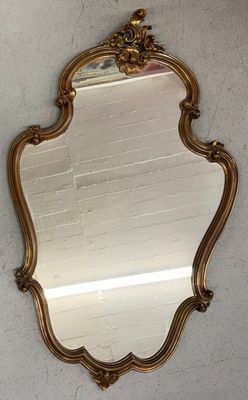 un miroir à cadre doré accroché à un mur blanc, avec un mur de briques en arrière-plan