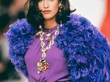 a woman that is walking down the runway wearing a purple jacket