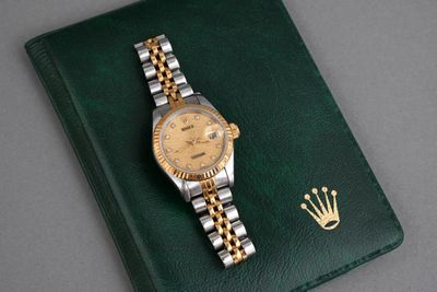 a watch on a green book with a gold crown on it